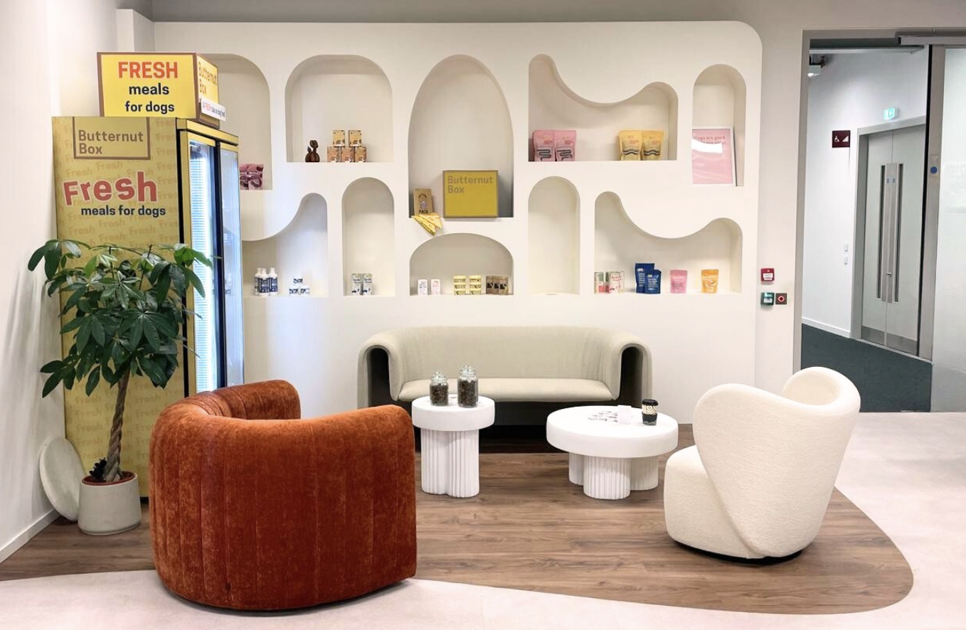 Butternut Box office reception area with curved white display wall, branded fridge, and comfortable seating area